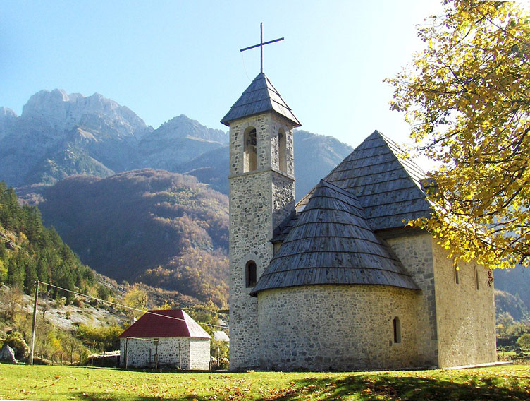 Historical Church of Theth on a sunny day surrounded by lush green nature of the Albanian Alps