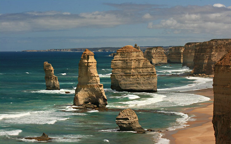 Photo of extraordinary wave-sculpted rock formations known as the Twelve Apostles on the shoreline by the beach.