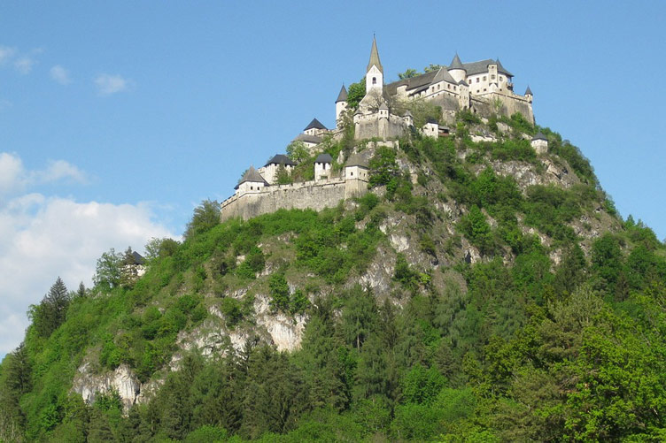 Hochosterwitz castle perched on top of a steep green mountain set against the blue sky. 