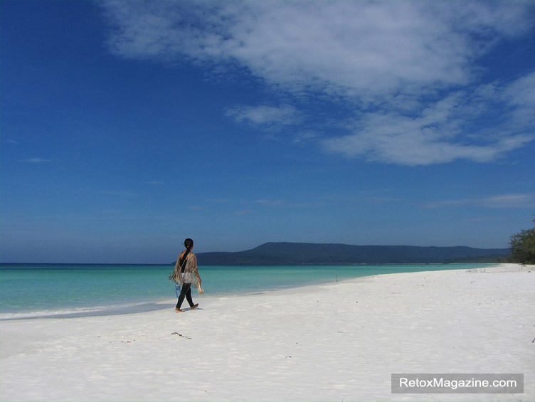 A person walking in the sun on the pristine white sand beach along the blue coastline on Koh Rong Island