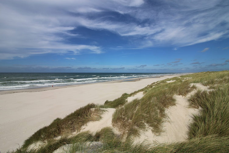 Sand dunes, beach, blue sea and a blue cloudy sky