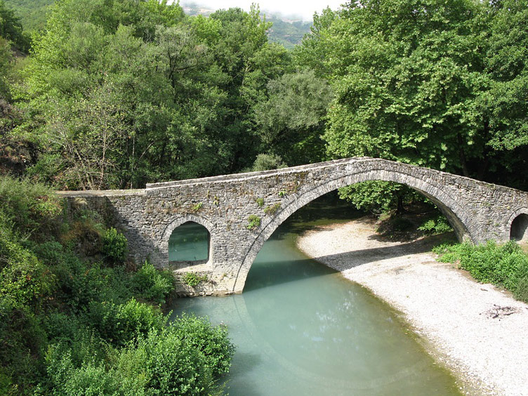 A bridge of a unique design style stretching over a river surrounded by trees