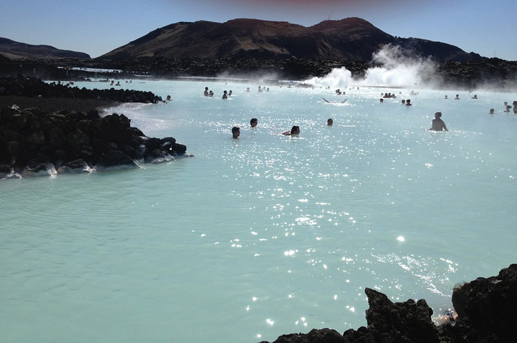 People dotted around swimming in the steaming blue lagoon surrounded by volcanic rock formations