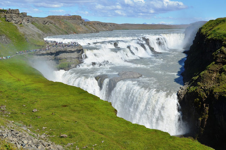 Gullfoss iconic foaming waterfall set against mountains and lush green grass