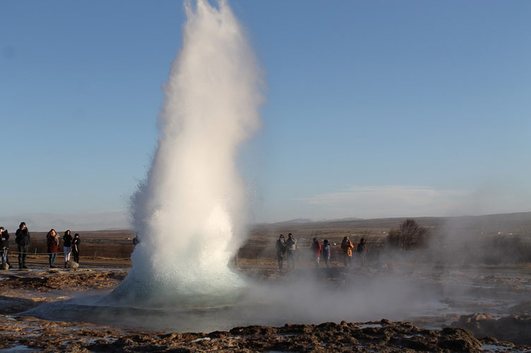 People observe as Strokkur fountain geyser spouts water high into the air