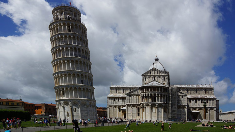 The Leaning Tower of Pisa next to Pisa Cathedral building at day time with people around