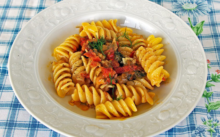 Italian pasta served on a plate topped with tomatoes and herbs.