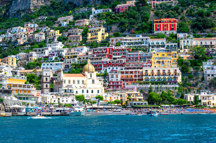 White and brightly coloured building of the picturesque village of Positano with blue seawater in front 