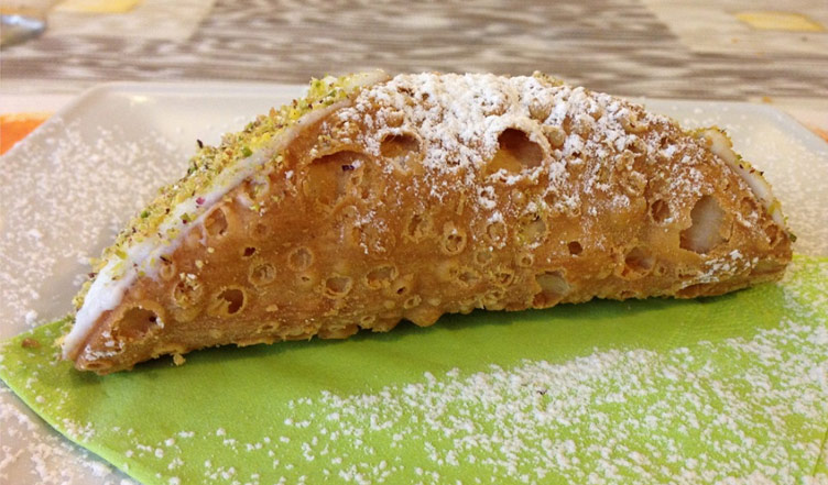 A side view of the Sicilian cannolo sweet from Italian cuisine. The sweet is very well presented with icing sugar frosting. 