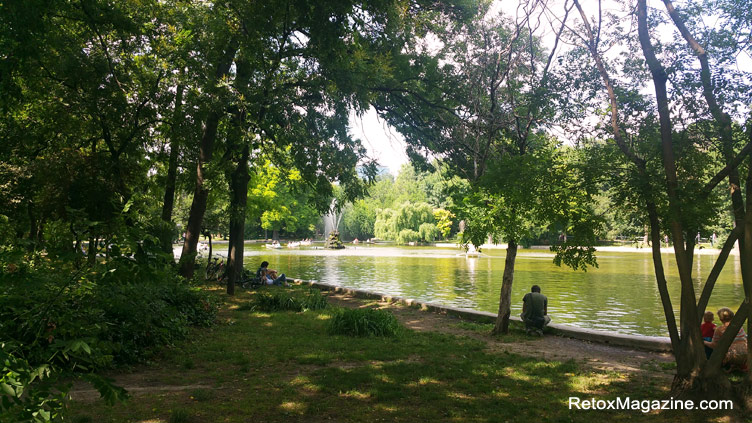 een fontein en meer omringd door weelderige groene natuur en mensen die chillen in Cismigiu Park in Boekarest