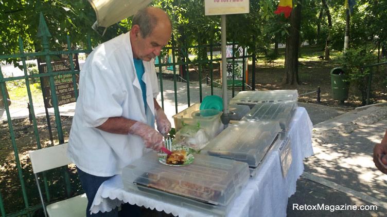 Um local romeno homem que vende doces caseiros e bolos sobre uma mesa ao lado de uma entrada para o parque