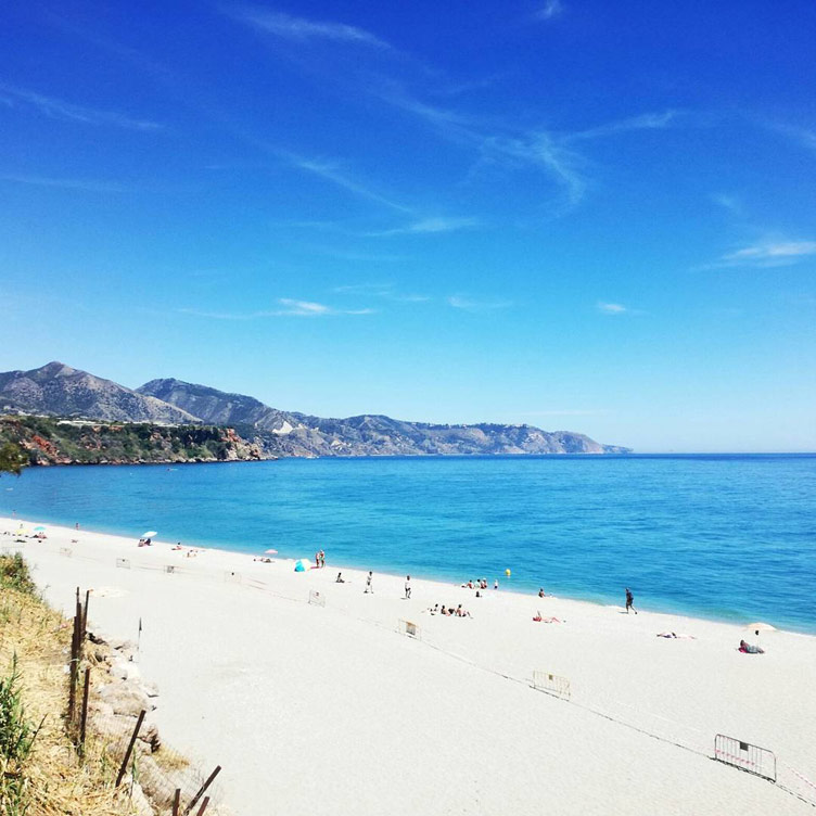 Light sand beach set against blue sea waters at Burriana Beach in Nerja, Spain