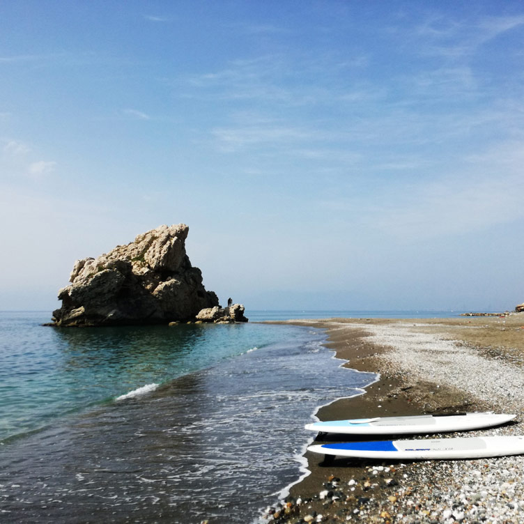 Two boards perfectly placed out of water on a Malaga beach, in the background is the beach, sea and a huge rock formation in the sea