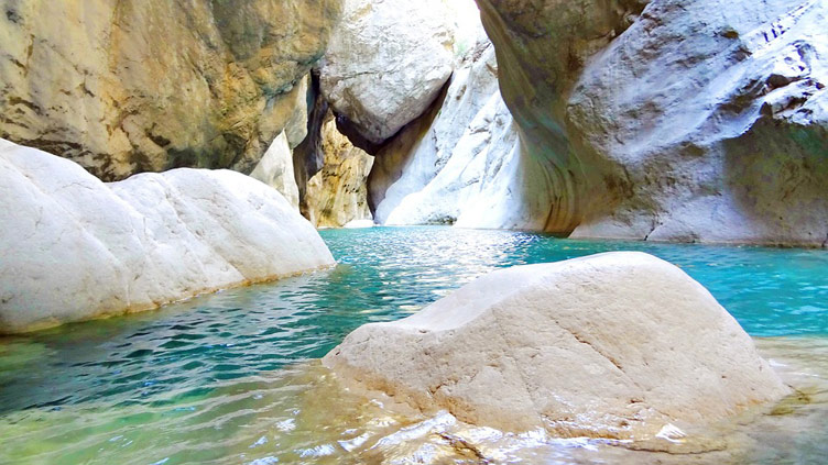 Visible are smooth rock formations on either side of clear turquoise-blue water passageway set in between the rocks 