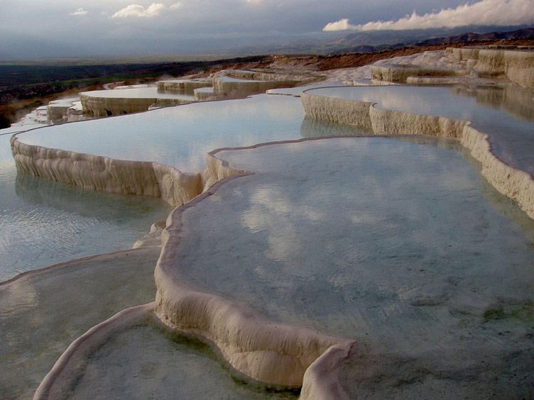 White multilevel travertine terraces holding crystal clear water reflecting the blue tones of dusk