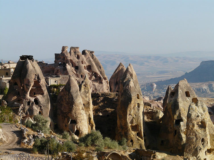 Many tall cone-like natural rock structures with rooms and windows carved into the rocks over multiple levels.