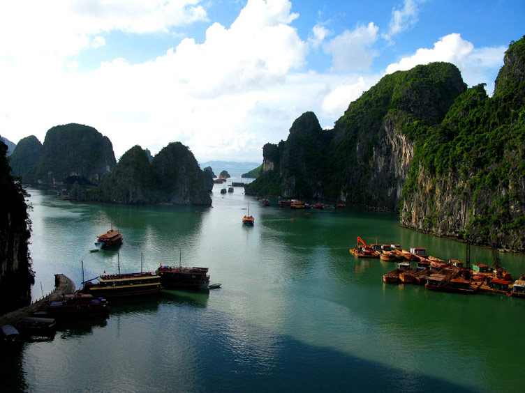 Boats in green sea water set against iconic rock formations of Ha Long Bay, photographed from above